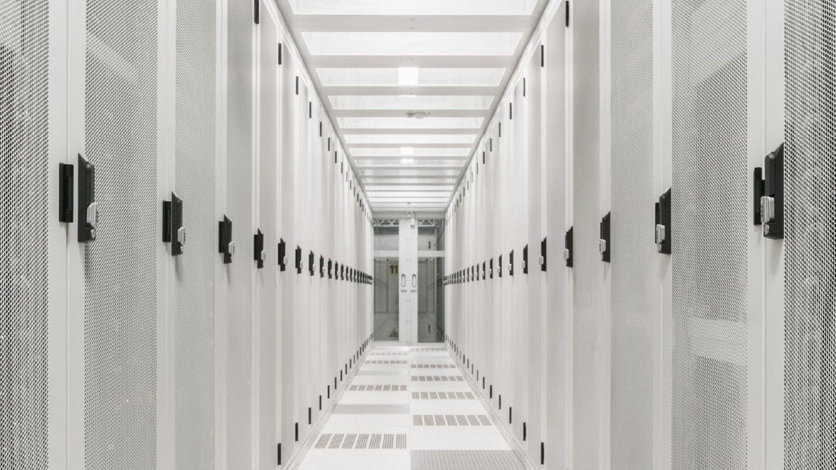 I’m inspecting the attached hero image so the alt text accurately describes its visible content.  A bright white server room corridor lined with rows of data center racks.