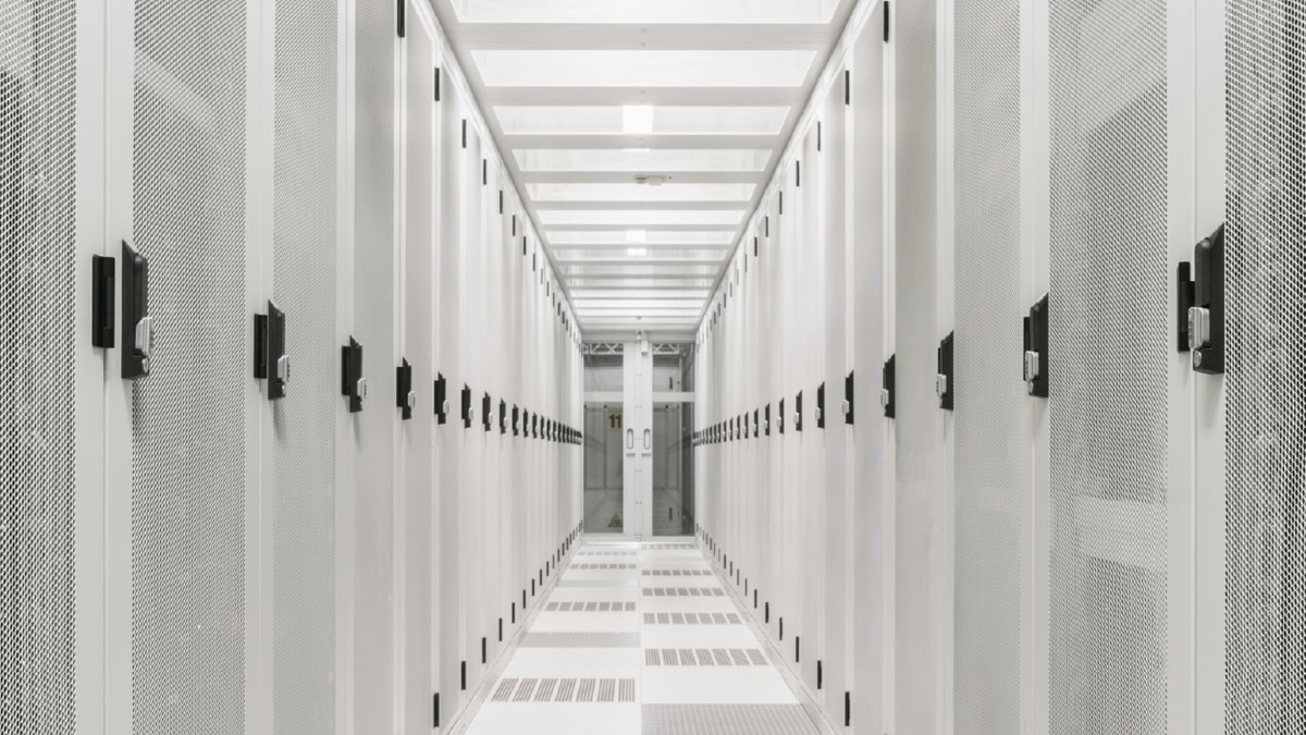 I’m inspecting the attached hero image so the alt text accurately describes its visible content.  A bright white server room corridor lined with rows of data center racks.